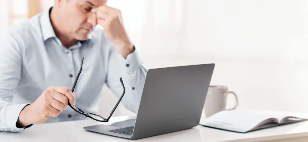 Exhausted senior manager massaging nose while using laptop